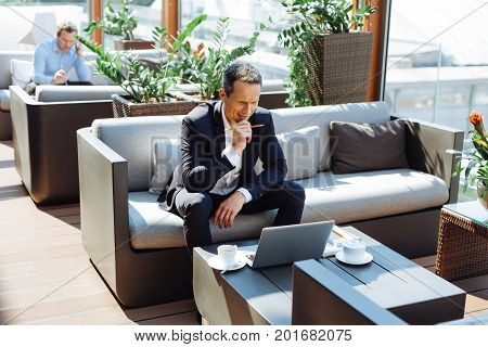 New solutions. Smart professional handsome entrepreneur holding a pencil and looking at the laptop screen while thinking about his problem