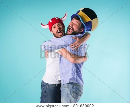 Two excited male friends celebrate watching sports on television over blue studio