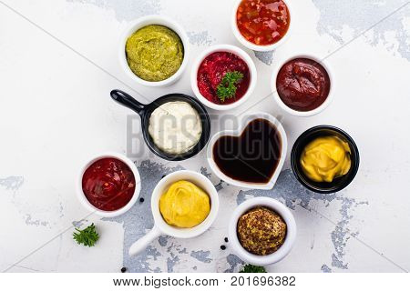 Various sauces and dips in porclean bowls on white stone background. Copy space