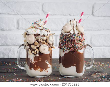 Close up view of two freakshake in mason jar on brown table. Freaked milkshake with chocolate, biscuit cookies and sugar sprinkling. Trendy food concept