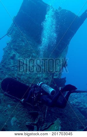 Scuba diver is exploring shipwreck, blue background.