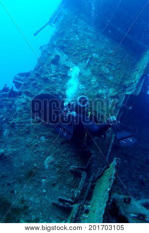 Scuba diver is exploring shipwreck, blue background.