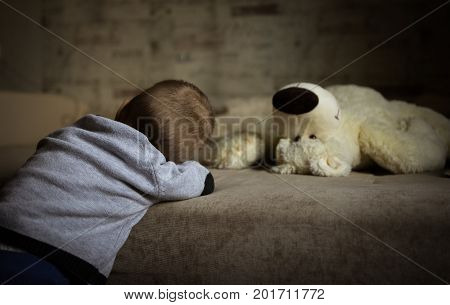 a little boy stands near the sofa on which lies a toy bear