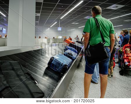 FRANKFURT GERMANY - AUG 8 2017: Exhausted passengers commuters waiting to claim the baggage luggage at modern airport looking at the luggage conveyor belt for their suitcase bag backpack