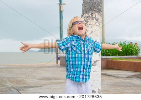 A cool blond boy in sunglasses screeming happyly in a park near beach