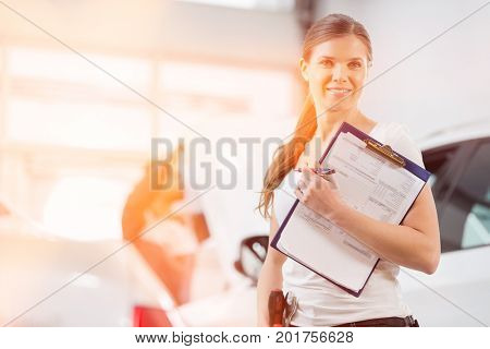 Portrait of smiling female repair worker with clipboard in car workshop