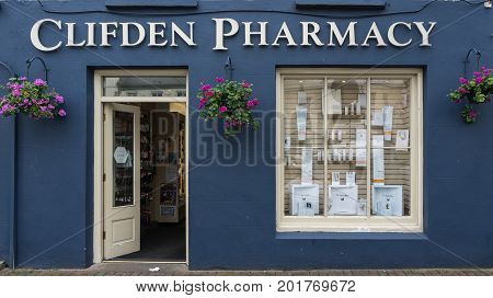 Clifden Ireland - August 4 2017: The dark blue facade of the small business pharmacy with white trim open door and display window. Street scene and flowers on the wall.