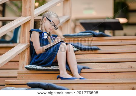 Adorable little school girl with notes and pencils outdoor.