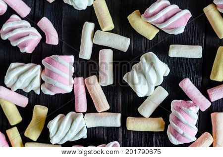 Multicolored Marshmallow Background on Black Wooden table. Background of multi-colored and different in shape and size of marshmallows. Sweets background