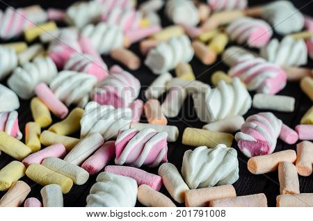 Multicolored Marshmallow Background on Black Wooden table. Background of multi-colored and different in shape and size of marshmallows. Sweets background