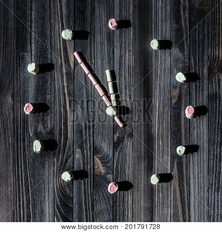 A dial of watches from white and pink marshmallows on a black wooden board background.