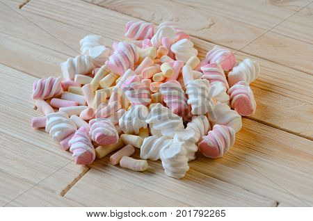 Multicolored marshmallows on bright wooden table. Background of multi-colored and different in shape and size of marshmallows. Sweets background