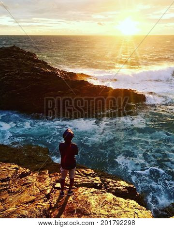 Boy looks at sunset over a rocky coastline. Quiberon, Britanny, France.