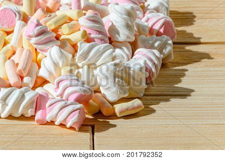 Multicolored marshmallows on bright wooden table. Background of multi-colored and different in shape and size of marshmallows. Sweets background
