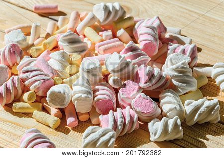 Multicolored marshmallows on bright wooden table. Background of multi-colored and different in shape and size of marshmallows. Sweets background
