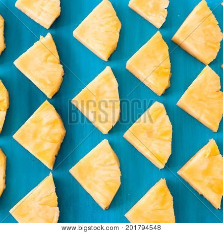 Close up patter of many pieces of yellow pineapple laying on blue wooden table background.