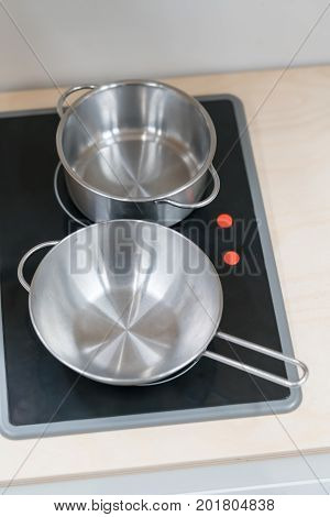 Mini stainless steel pot and pan on black electric stove over wooden countertop. Simple kitchenware toy model for kid role play.