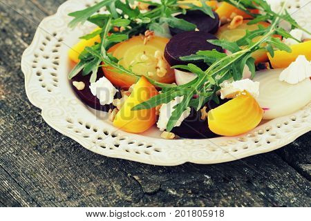 Healthy Beet Salad with red, white, golden beets, arugula, nuts, feta cheese on wooden background .