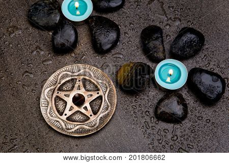 Turquoise Candles With Black Rocks And Silver Pentagram On Gray Slate Background With Water Droplets