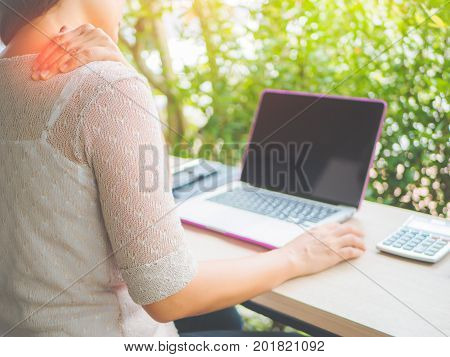 Woman put her hand on the back of her neck while feeling pain after long hours work on computer. Office syndrome concept.