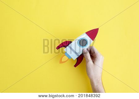 Hand Holding Rocket Spaceship on Yellow Background