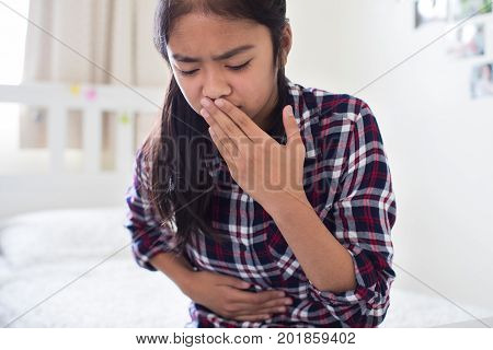 Young Girl Sitting On Bed At Home Feeling Nauseous