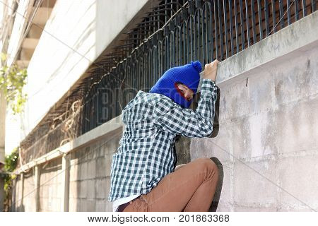 Masked burglar climbs through a fence. Catch burglar concept