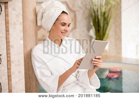 attractive woman in bath robe relaxing after spa pedicures and using digital tablet