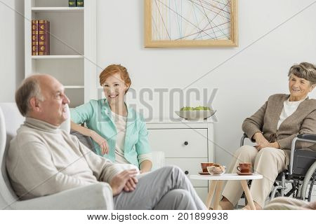 Young assistant talks with two elder people in retirement home