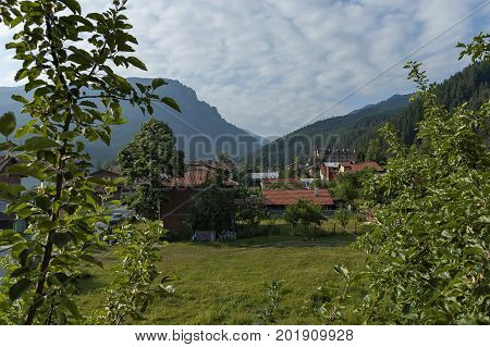 Scene with mountain top, forest, glade and residential district of bulgarian village Beli Iskar, Rila mountain, Bulgaria