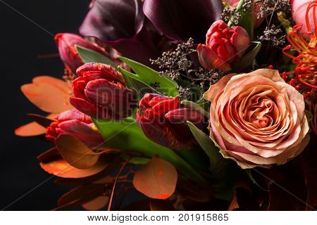 Colorful fall bouquet on black background. Autumn composition of roses, tulips, dry leaves and herbs closeup. Flower shop and florist design concep