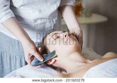 Young woman have face guasha treatment at asian beauty clinic