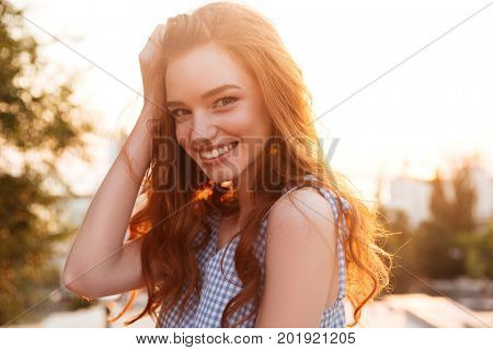 Close up picture of a Beauty Smiling Ginger girl in dress posing sideways on the sunset and looking at the camera