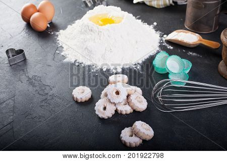 Flour eggs and canestrelli Italian shortbread cookies cooking utensils on black table