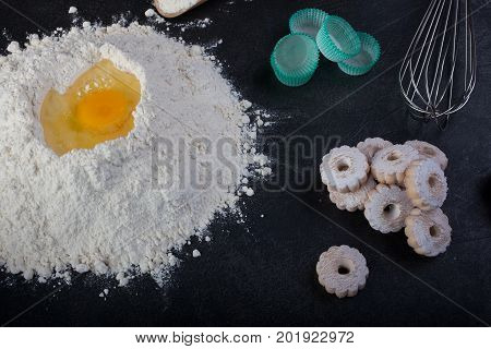 Flour eggs and canestrelli Italian shortbread cookies cooking utensils on black table