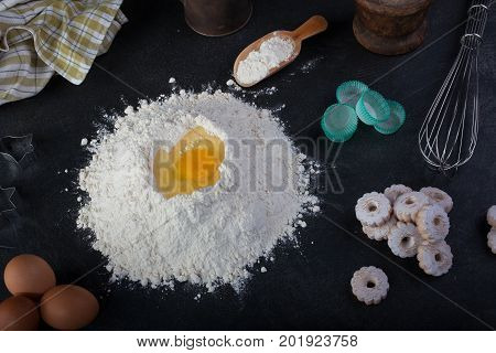 Flour eggs and canestrelli Italian shortbread cookies cooking utensils on black table
