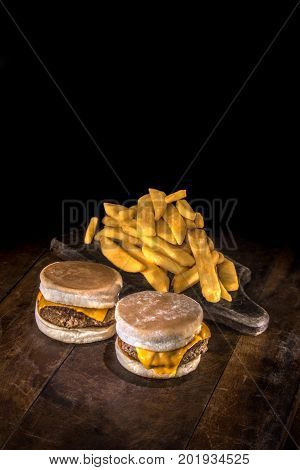 Two mini delicious hamburgers with melted cheddar and fried potato on a dark wood background
