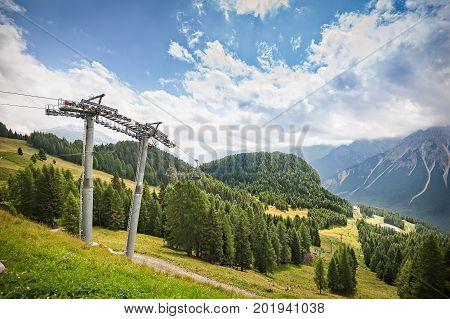 Mountain panorama with forest Dolomites valley and chairlift in summer. Sky with clouds.