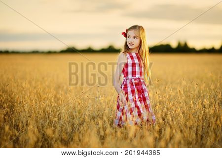 Adorable Girl Walking Happily In Wheat Field On Warm And Sunny Summer Evening