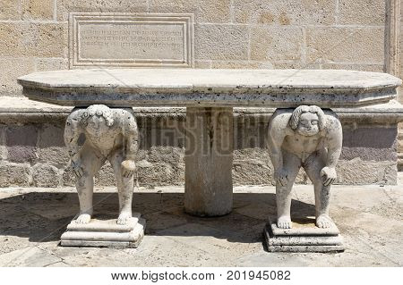 PERAST, MONTENEGRO - AUGUST 04, 2017:Stone table with male figures near the church on the island of Gospa od Skrpela in the Boko-Kotorsky Gulf. Montenegro.