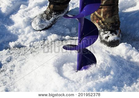 Drilling An Ice Fishing Hole With A Boots In The Background