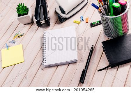Top view workspace mockup on wooden background with blank notebook with copy space, pen, tacker, punch, clips and accessories. Overhead view. Flat lay, top view
