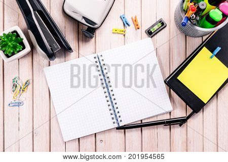 Top view workspace mockup on wooden background with blank notebook with copy space, pen, tacker, punch, clips and accessories. Overhead view. Flat lay, top view