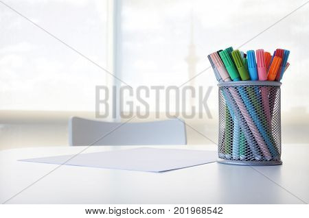 Colourful pens and blank white paper on a table with chair. Creativity concept. Copy space