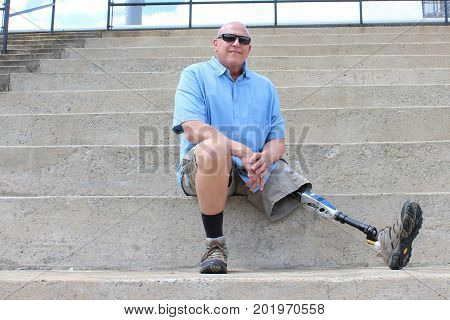 Seated man with prosthetic leg outstretched, on concrete bleachers