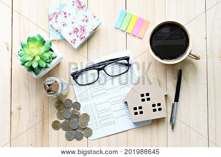 Business, finance, saving money, banking, property loan or mortgage concept : Top view or flat lay of saving account book or financial statement, wood house model and coins on office desk table