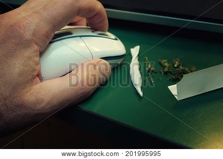 Marijuana joint laid on the desk and human hand with computer mouse closeup photo