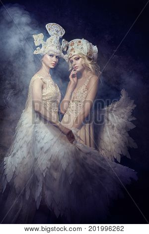 Angel nymph fairy art pictures of women. Girls with angel wings beauty models posing on a dark background. Fairy tale magic magical girl in gorgeous expensive dresses