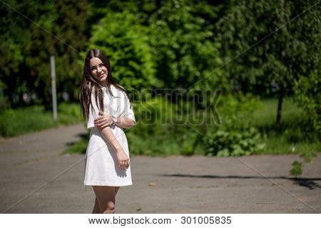 Young Smiling Brunette Woman In The Park Touching Her Right Hand With Her Left Hand. She Is Wearing 