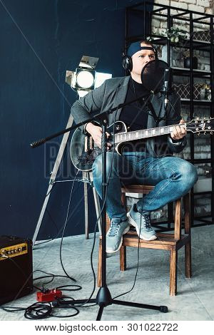 Close Up Of A Man Singer Sitting On A Stool In A Headphones With A Guitar Recording A Track In A Hom